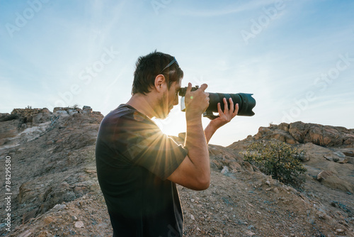 Side view of man photographing with camera at desert at sunset photo