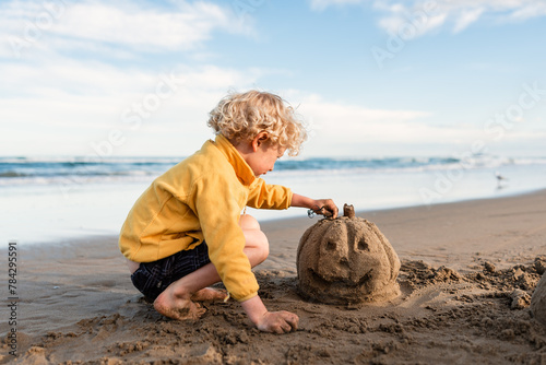 Curly haired child building a sand Jack-o-Lantern at beach