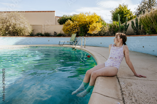 Tween girl sitting on side of pool looking away photo