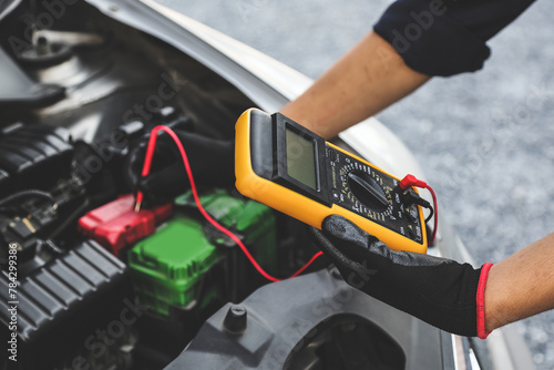 Hand car mechanic holding voltmeter to check voltage car battery energy problem for service maintenance and re charger or jump start or change battery replacement. photo