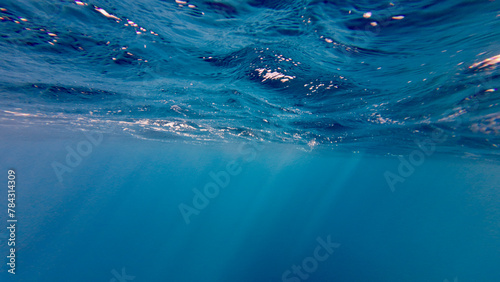 Sun rays under water. The sun's rays pass through waves on the surface of the ocean. Sun rays in the thickness of transparent water on a blue background.