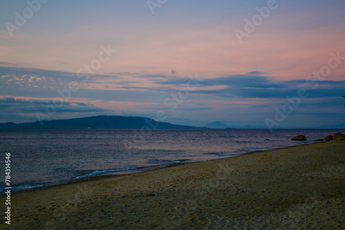 Sea and sandy beach at dusk. View of the beach  calm sea and tropical island on the horizon in the evening.