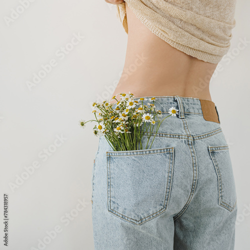 Backside view of young pretty woman. Chamomile flowers bouquet in jeans pocket © Floral Deco