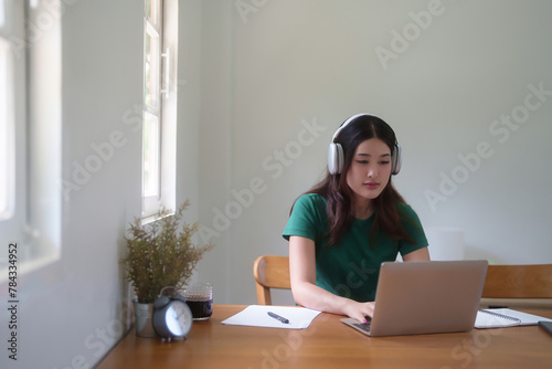 Young asian student women wear headphone to studying and watching lecture webinar in online class on laptop while typing to researching information and learning knowledge remote education from home