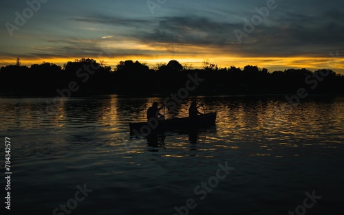 Silhouette of fishermen pedalling their boat at sunset cloudy golden sky background