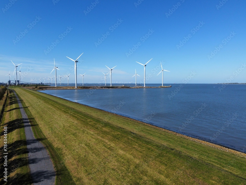 Aerial view of the blue sea and green shoreline with wind turbines in the background.
