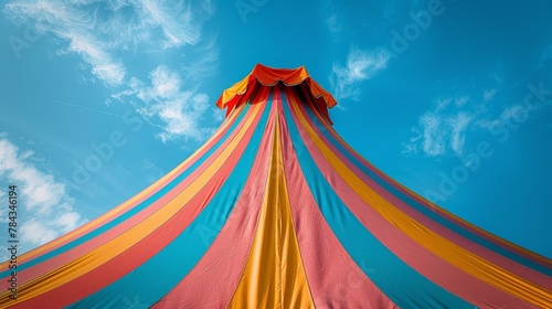 Looking up, the colorful stripes of a circus tent peak majestically against a bright blue sky, embodying the joyful spirit of the circus.