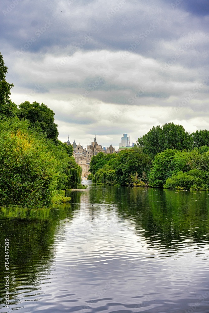 Vertical of a tranquil lake surrounded by green trees in a park on a cloudy day Vertical of a tranquil lake surrounded by green trees in a park on a cloudy day