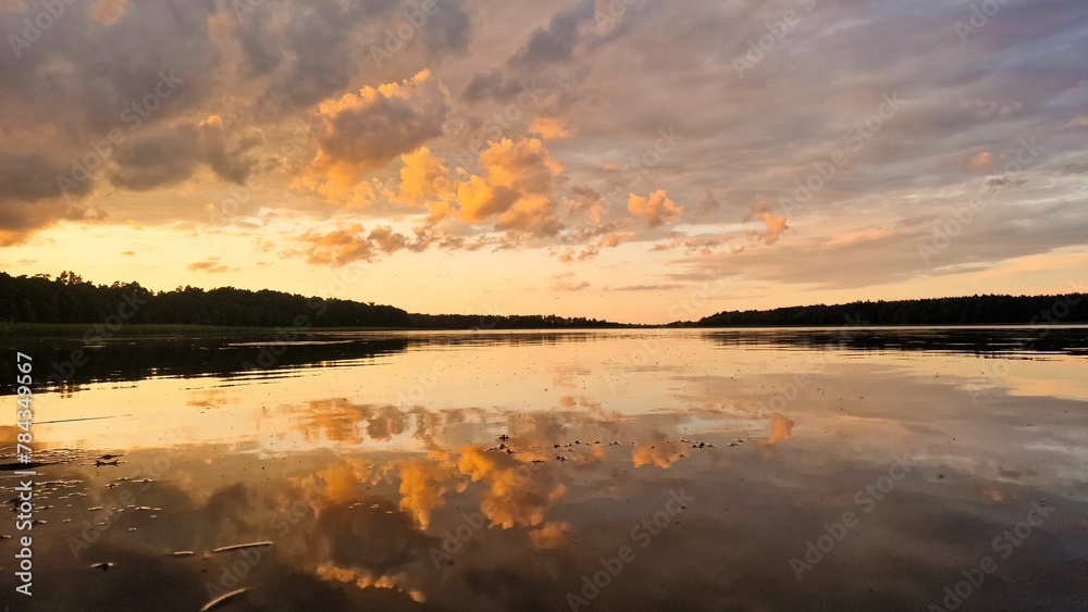 Fototapeta premium Reflection of fluffy clouds in the sunset sky on the scenic surface of a mirror lake in Poland