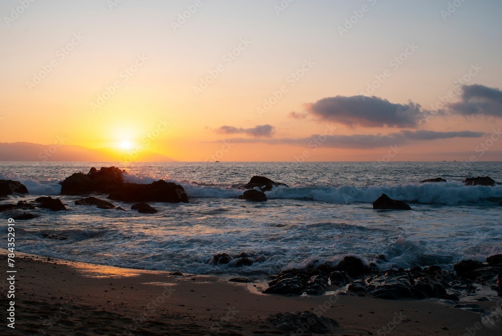 Obraz premium Red sunset view over a seascape with clear sky and sun in the background stones around