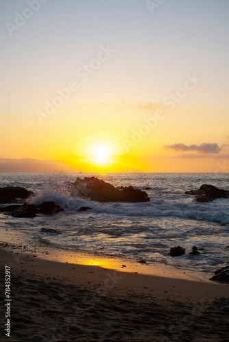Red sunset view over a seascape with clear sky and sun in the background stones around