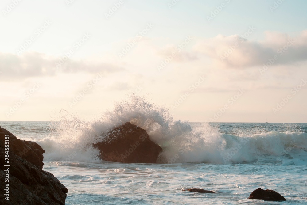 Obraz premium Seascape view with water waves hitting on rocky cliffs, sunlit sky background