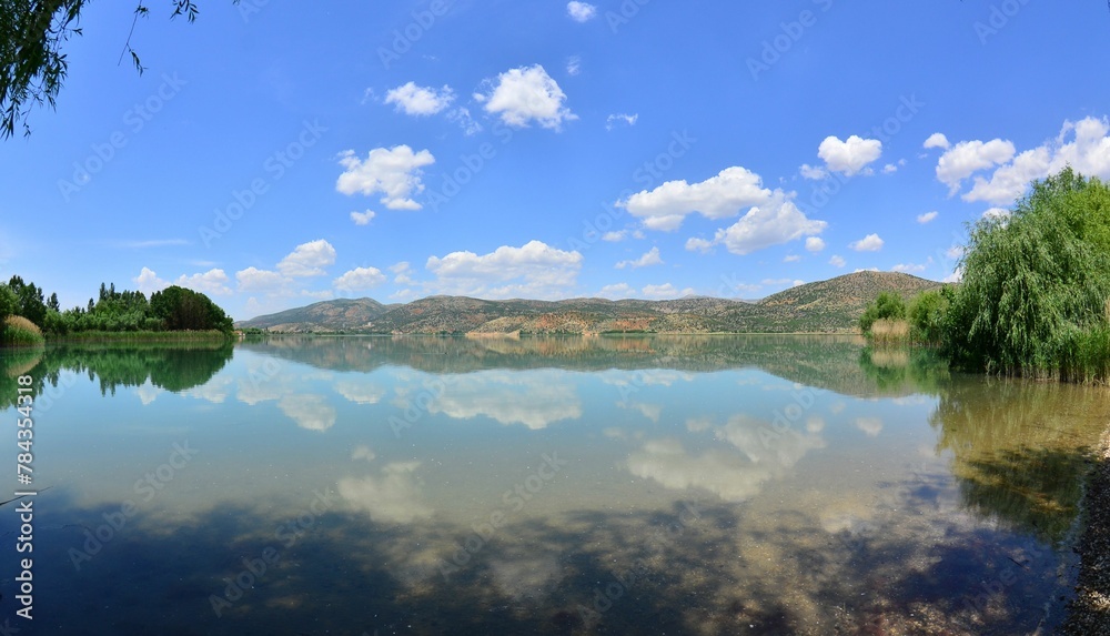 Obraz premium Beautiful lake reflecting the green trees on the shore and a cloudy sky in the background