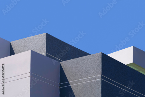 High section of gray and white buildings group in geometric shape with sunlight and shadow on surface against blue clear sky background, Exterior architecture in minimal style © Prapat