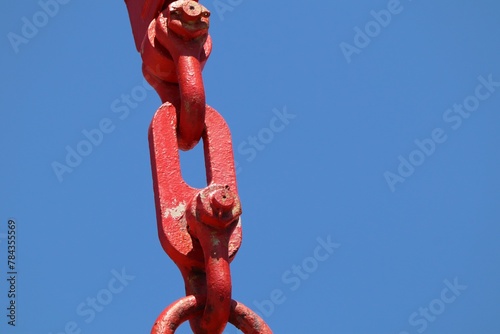 Close-up shot of a red crane chain against a blue sky in the sunlight