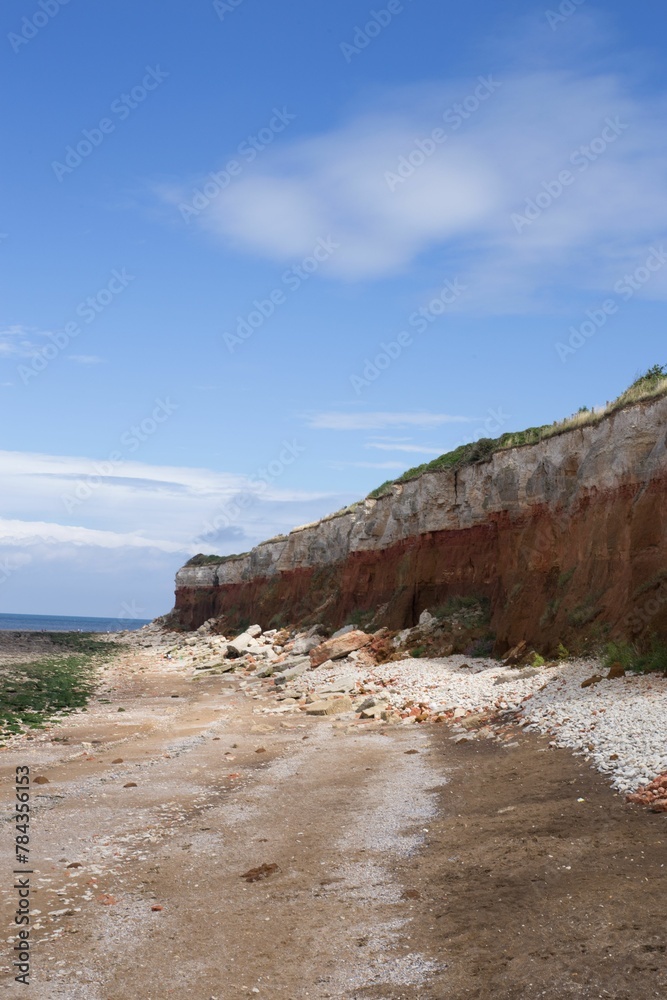 Vertical shot of a cliff next to the sea with the blue sky in the background
