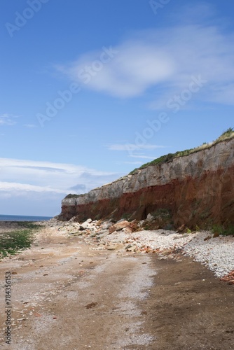 Vertical shot of a cliff next to the sea with the blue sky in the background