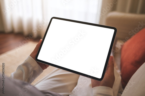 Mockup image of a woman holding digital tablet with blank desktop screen while sitting on sofa at home