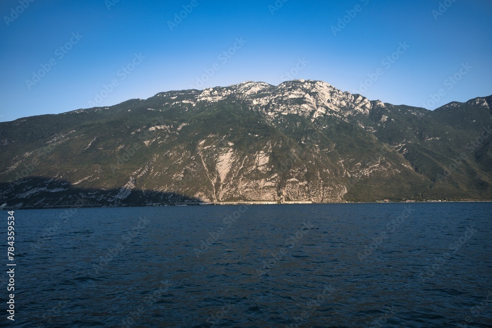 Landscape of lake Garda surrounded by hills under a blue sky and sunlight in Italy