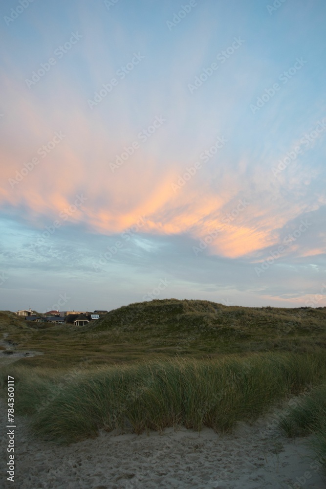 Fototapeta premium Grass terrain with houses and hills against the colorful sky during a sunset in Ringkobing, Denmark