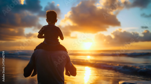 Rearview silhouette of a father carrying his son on back or shoulders, dad holding toddler boy around his neck, watching sunset over sea or ocean water. Family vacation, parent and child, copy space photo