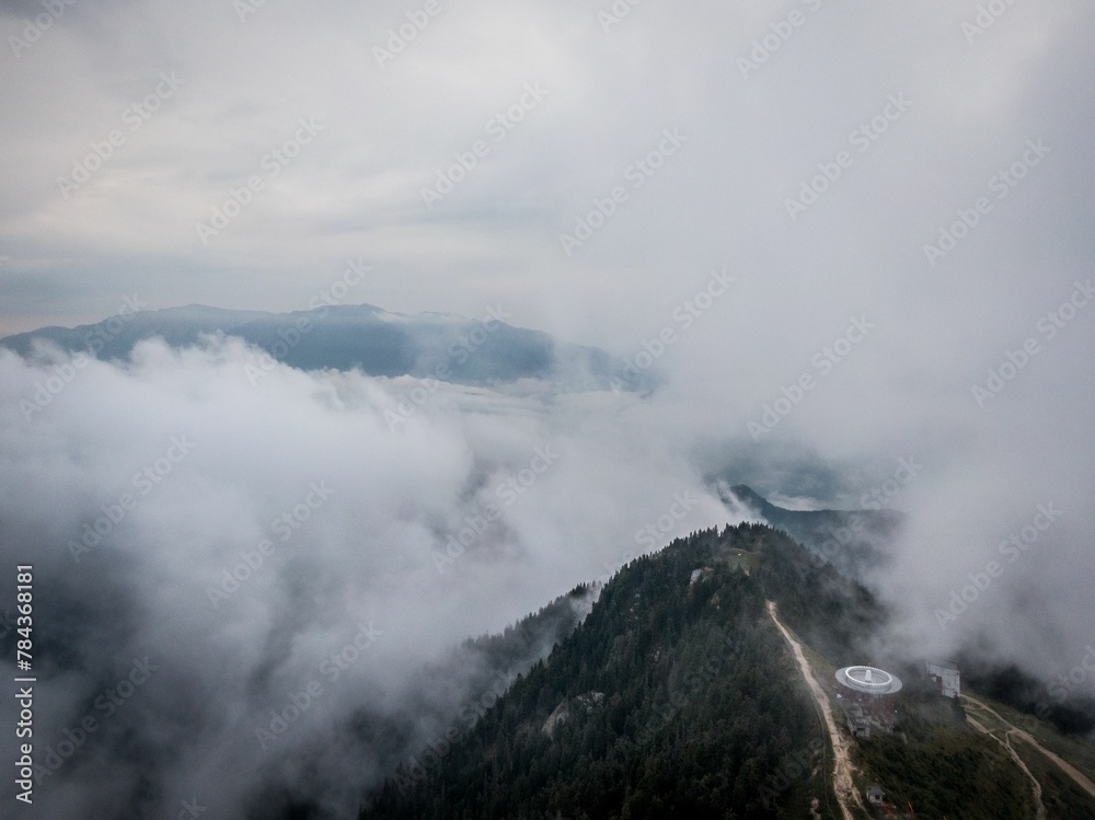 Aerial view of a dense green mountain forest covered with dense fog on a cloudy day