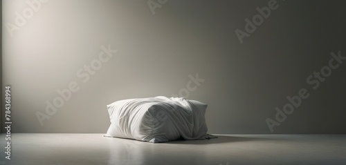 A single white pillow wrapped tightly in cloth, sitting isolated on a grey floor, giving a surreal artistic impression.