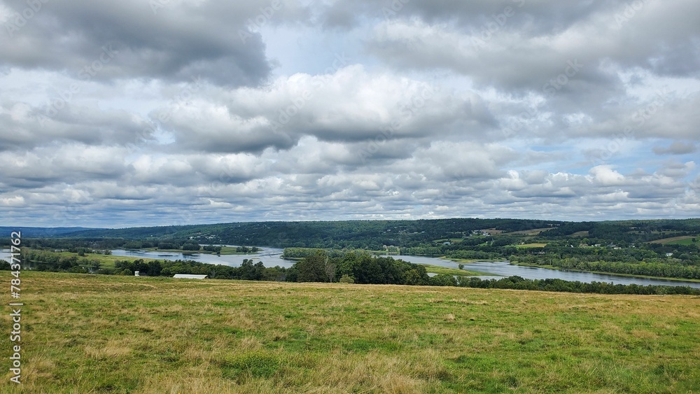 Grassy field with a river in the distance against the cloudy sky