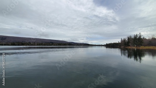 View of a lake before the coastline with hills and trees under the cloudy sky in Cape Breton