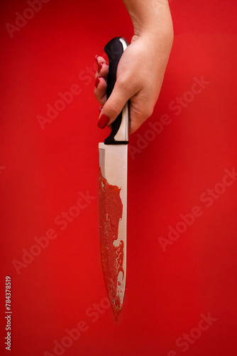 Close up of a female hand holds a bloodied knife. Red blood runs down it. Bright red background. Creep horror stories. © Dasha Petrenko