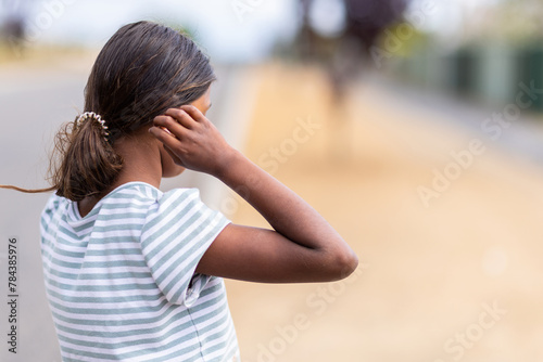 young aboriginal girl standing side-on incognito with hand to head