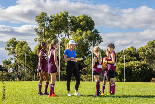 female coach holding clipboard addressing schoolchildren in sports uniforms photo