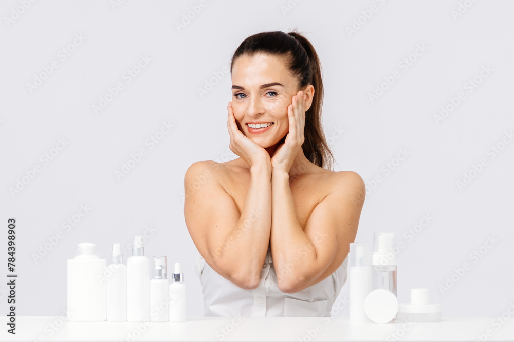 Portrait of a happy attractive middle-aged woman next to mock-ups of jars with cream and cosmetology natural cosmetics. Advertising of spa treatments, anti-aging care products for delicate dry skin.