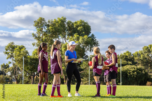 sports teacher addressing a group of children on football field photo