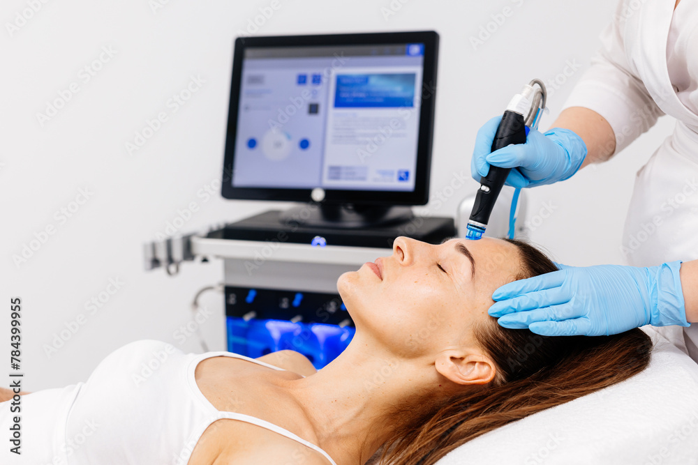 Fototapeta premium Close-up of a cosmetologist's hands polishing and cleansing the skin of a middle-aged woman's face using a vacuum machine. Concept of skin care, rejuvenation and cosmetology.