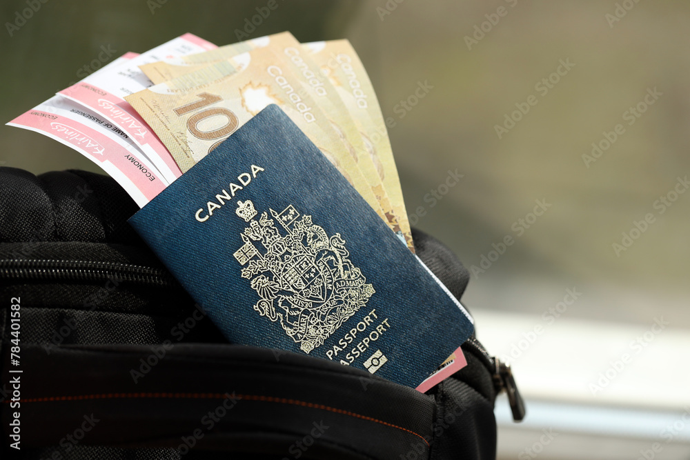 Fototapeta premium Canadian passport and dollar money bills with airline tickets on backpack close up