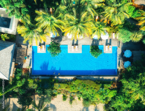 Aerial view of swimming pool, sunbeds and umbrellas, green palms, sandy beach in luxury resort at sunset in summer. Nungwi, Zanzibar island. Top drone view. Tropical landscape. Exotic. Sea coast