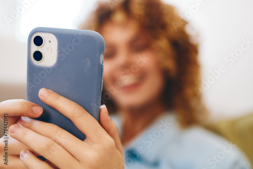 Happy woman holding mobile phone and enjoying online games on cozy sofa at home