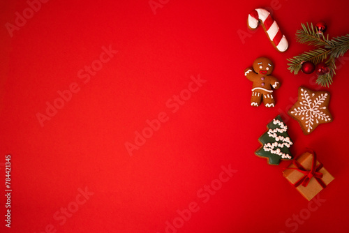 Cute red holiday background with cookies, sprig of fir tree with Christmas balls and a gift in craft paper. Cookies in the form of a gingerbread man, a Christmas tree, stars and a candy cone.