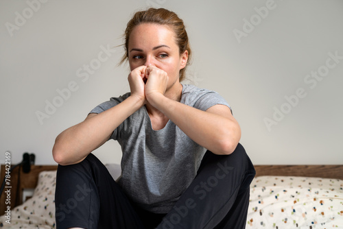 Downcast and depressed adult woman at home. Unhappy female person sits on the bed at home. 