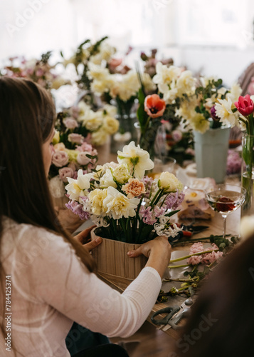 Over-the-shoulder view of a floristry session with hands arranging an intricate mix of pastel flowers in a wooden container.