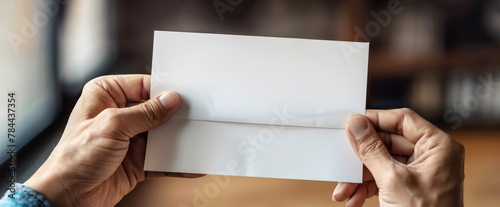 Senior person holds blank folded paper on blurry background closeup. Mature immigrant receives letter from relatives stayed in native country.