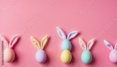 Holiday Easter background of colorful pastel Easter eggs and bunny ears on pink table top view