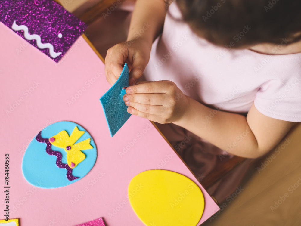 Hands of a little caucasian girl holding a blue sticker and peeling off a hat for felt eggs Hands of a little caucasian girl holding a blue sticker and peeling off a hat for felt eggs