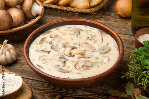 Cream of mushroom soup in a terracotta clay bowl with ingredients on a wooden rustic table.