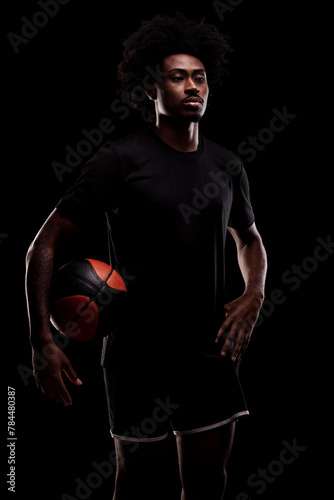 Basketball player holding a ball. Young african american sports man against black background.