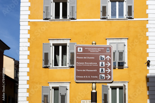 Tourist brown sign in a sunny day in Trento city center. Defocused yellow building in the background; Trentino-Alto Adige, Italy