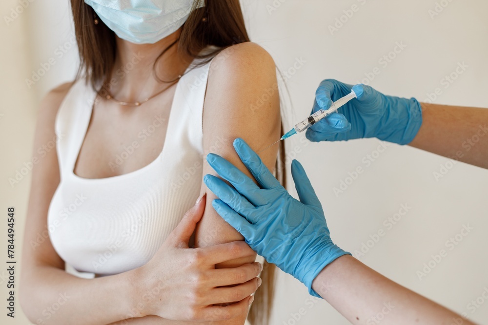 Woman in mask receiving an injection in her arm Woman in mask receiving an injection in her arm