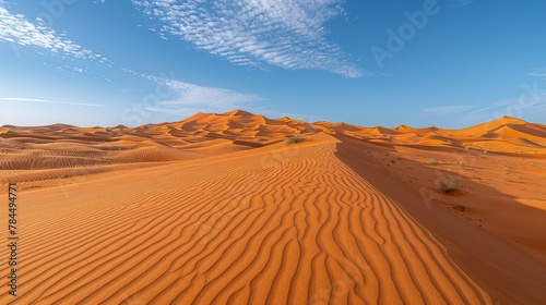   A vast expanse of sand dunes beneath a blue sky with wisps of clouds