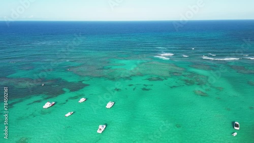 Drone gracefully glides above breathtaking coral barrier reef and yachts in Caribbean Sea, illuminated by soft sunlight. Turquoise water